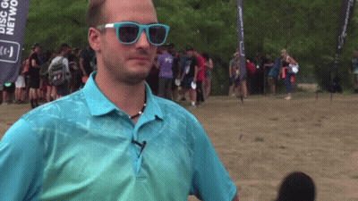 A Man Wearing Sunglasses Stands In Front Of A Banner That Says Disc Golf GIF