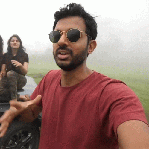 A Man Wearing Sunglasses Stands In Front Of A Car With A Woman In The Background GIF