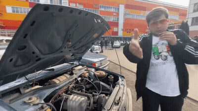 A Man Wearing Sunglasses Stands In Front Of A Car With The Hood Open And The Engine Exposed GIF