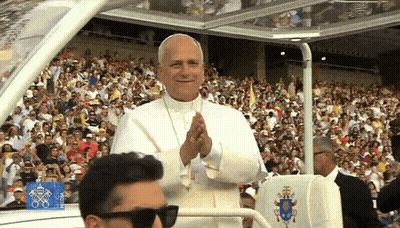 A Man Wearing Sunglasses Stands In Front Of A Crowd Of People While The Pope Applauds In The Background GIF