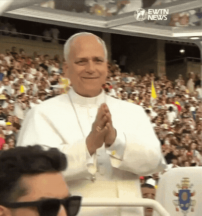 A Man Wearing Sunglasses Stands In Front Of A Crowd With Ewtn News Written On The Bottom Right GIF