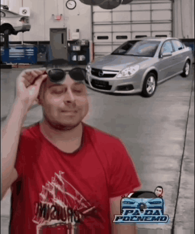 A Man Wearing Sunglasses Stands In Front Of A Garage Door With A Car In The Background GIF
