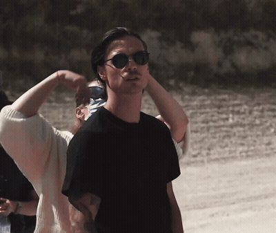 A Man Wearing Sunglasses Stands In Front Of A Woman GIF