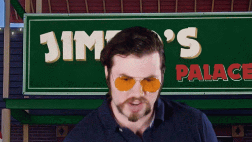 A Man Wearing Sunglasses Stands In Front Of Jimpo 'S Palace Sign GIF