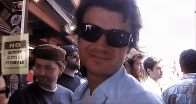 A Man Wearing Sunglasses Stands Next To A Sign That Says No Outside Alcohol Permitted GIF