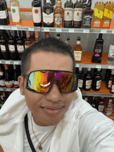 A Man Wearing Sunglasses Takes A Selfie In Front Of A Shelf Of Alcohol Including Jack Daniel 'S GIF