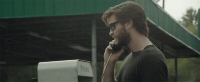A Man Wearing Sunglasses Talks On A Pay Phone GIF
