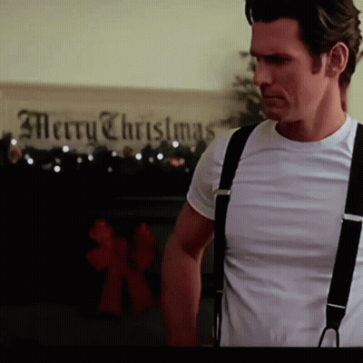 A Man Wearing Suspenders Stands In Front Of A Merry Christmas Sign GIF