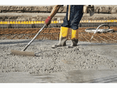 A Man Wearing Yellow Boots Is Raking Concrete On A Construction Site GIF