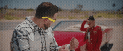 A Man Wearing Yellow Sunglasses Stands Next To A Woman In A Red Dress GIF