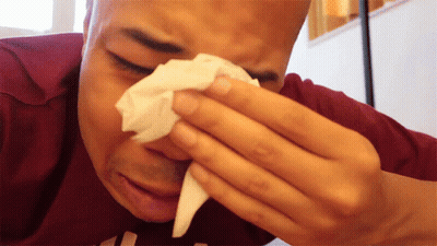 a man wipes his nose with a tissue while wearing a maroon shirt with the letter h on it