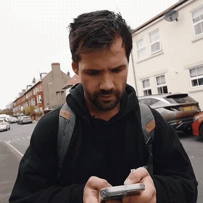 A Man With A Backpack Is Looking At His Cellphone GIF