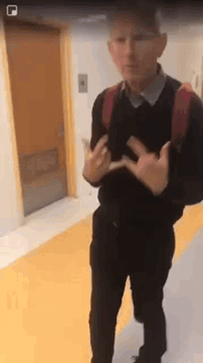 A Man With A Backpack Is Standing In A Hallway Making A Peace Sign With His Hands . GIF