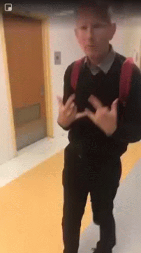 A Man With A Backpack Is Standing In A Hallway With His Hands Outstretched . GIF