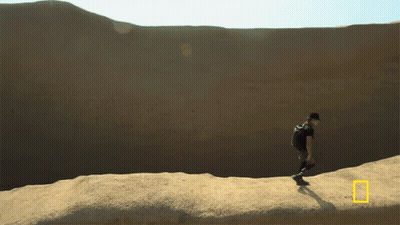 A Man With A Backpack Is Walking Across A Desert Landscape GIF