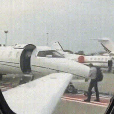 A Man With A Backpack Is Walking Towards A White Airplane . GIF