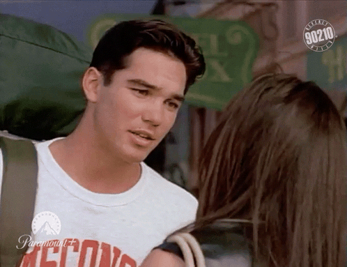 A Man With A Backpack Talks To A Woman With A 90210 Logo In The Corner GIF