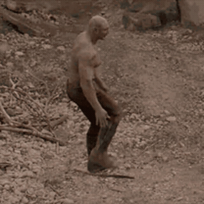 A Man With A Bald Head Is Standing In The Dirt Holding A Sword . GIF