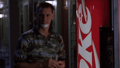 A Man With A Bandage Around His Mouth Stands In Front Of A Coke Machine GIF