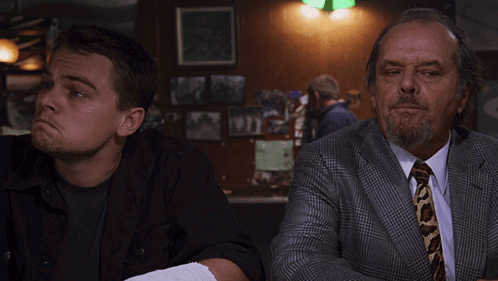 A Man With A Bandage On His Arm Sits Next To A Man In A Suit And Tie GIF