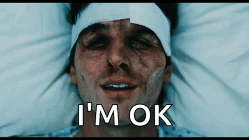 A Man With A Bandage On His Head Is Laying In A Hospital Bed With The Words I 'M Ok Below Him GIF