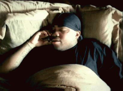 A Man With A Bandana On His Head Is Laying In Bed Talking On A Cell Phone GIF