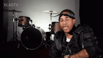 A Man With A Bandana On His Head Is Sitting In Front Of A Drum Set In A Room . GIF
