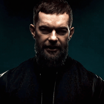 A Man With A Beard And A Black Jacket Is Looking At The Camera GIF
