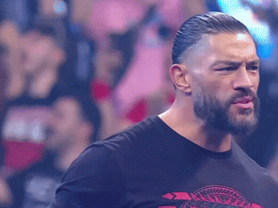 A Man With A Beard And A Black Shirt Is Standing In Front Of A Crowd And Making A Funny Face . GIF