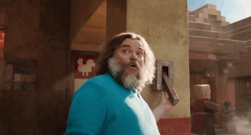 A Man With A Beard And A Blue Shirt Is Holding A Block GIF