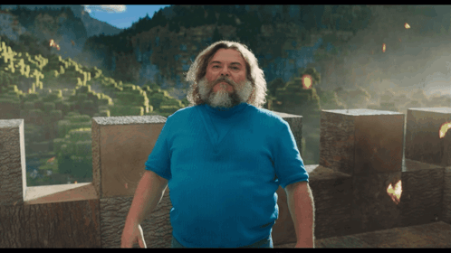 A Man With A Beard And A Blue Shirt Stands In Front Of A Mountain GIF