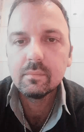A Man With A Beard And A Chain Around His Neck Is Looking At The Camera GIF