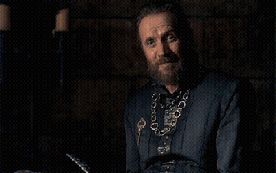 A Man With A Beard And A Chain Around His Neck Is Sitting In A Dark Room . GIF