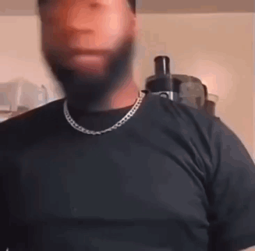 A Man With A Beard And A Chain Around His Neck Is Wearing A Black Shirt And A Black T-Shirt . GIF