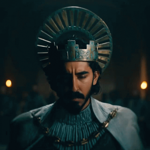 A Man With A Beard And A Crown On His Head Looks At The Camera GIF