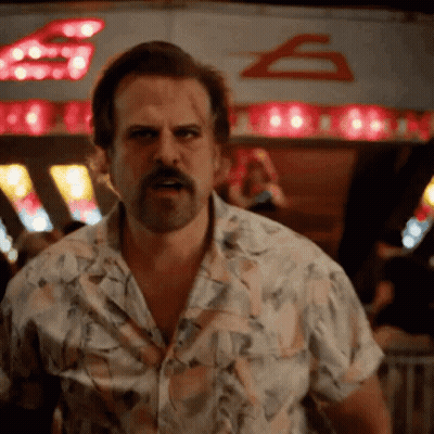 A Man With A Beard And A Floral Shirt Is Standing In Front Of A Sign That Says ' S ' On It GIF