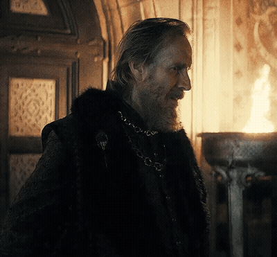 A Man With A Beard And A Fur Coat Is Standing In Front Of A Fire GIF
