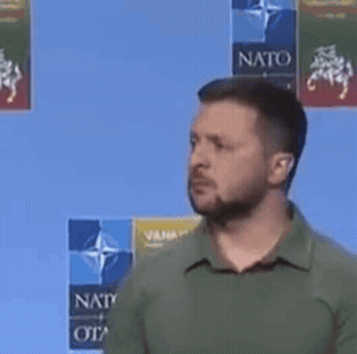 A Man With A Beard And A Green Shirt Is Standing In Front Of A Blue Background . GIF