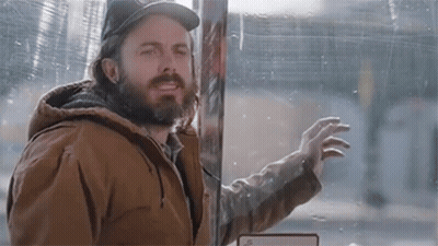 A Man With A Beard And A Hat Is Standing In Front Of A Glass Door . GIF