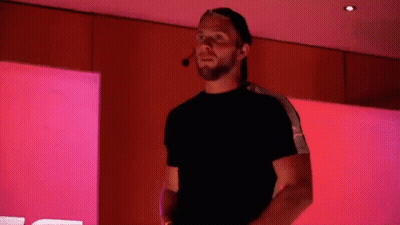 A Man With A Beard And A Hat Is Standing In Front Of A Pink Wall . GIF