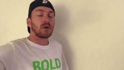 A Man With A Beard And A Hat Is Wearing A White T-Shirt That Says `` Bold '' . GIF