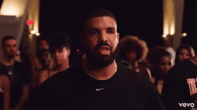 A Man With A Beard And A Nike Shirt Is Standing In Front Of A Crowd Of People . GIF
