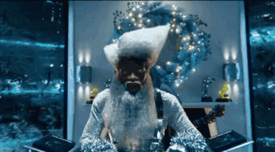 A Man With A Beard And A Santa Hat Is Sitting In Front Of A Wreath GIF