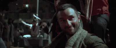 A Man With A Beard And A Scarf Around His Neck Is Standing In The Dark GIF