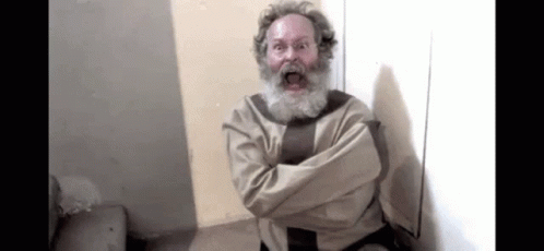 A Man With A Beard And A Straitjacket Is Sitting In A Room With His Arms Crossed . GIF