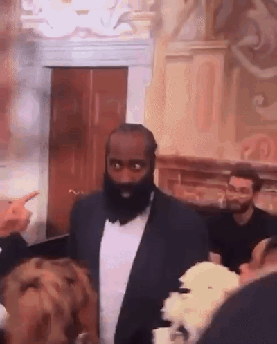 A Man With A Beard And A Suit Is Standing In A Room With People . GIF