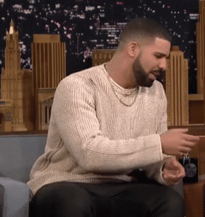 A Man With A Beard And A Sweater Is Sitting On A Couch . GIF