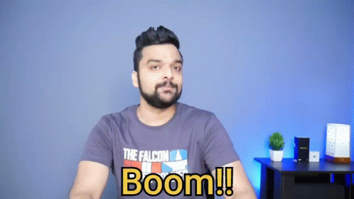 A Man With A Beard And A T-Shirt That Says Boom Is Sitting In Front Of A Blue Wall . GIF