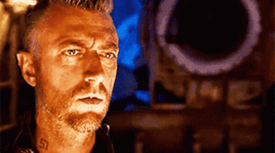 A Man With A Beard And A Tattoo On His Neck Is Standing In Front Of A Speaker . GIF