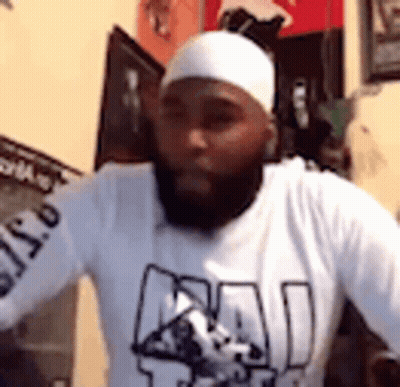 A Man With A Beard And A White Headband Is Wearing A White Shirt . GIF